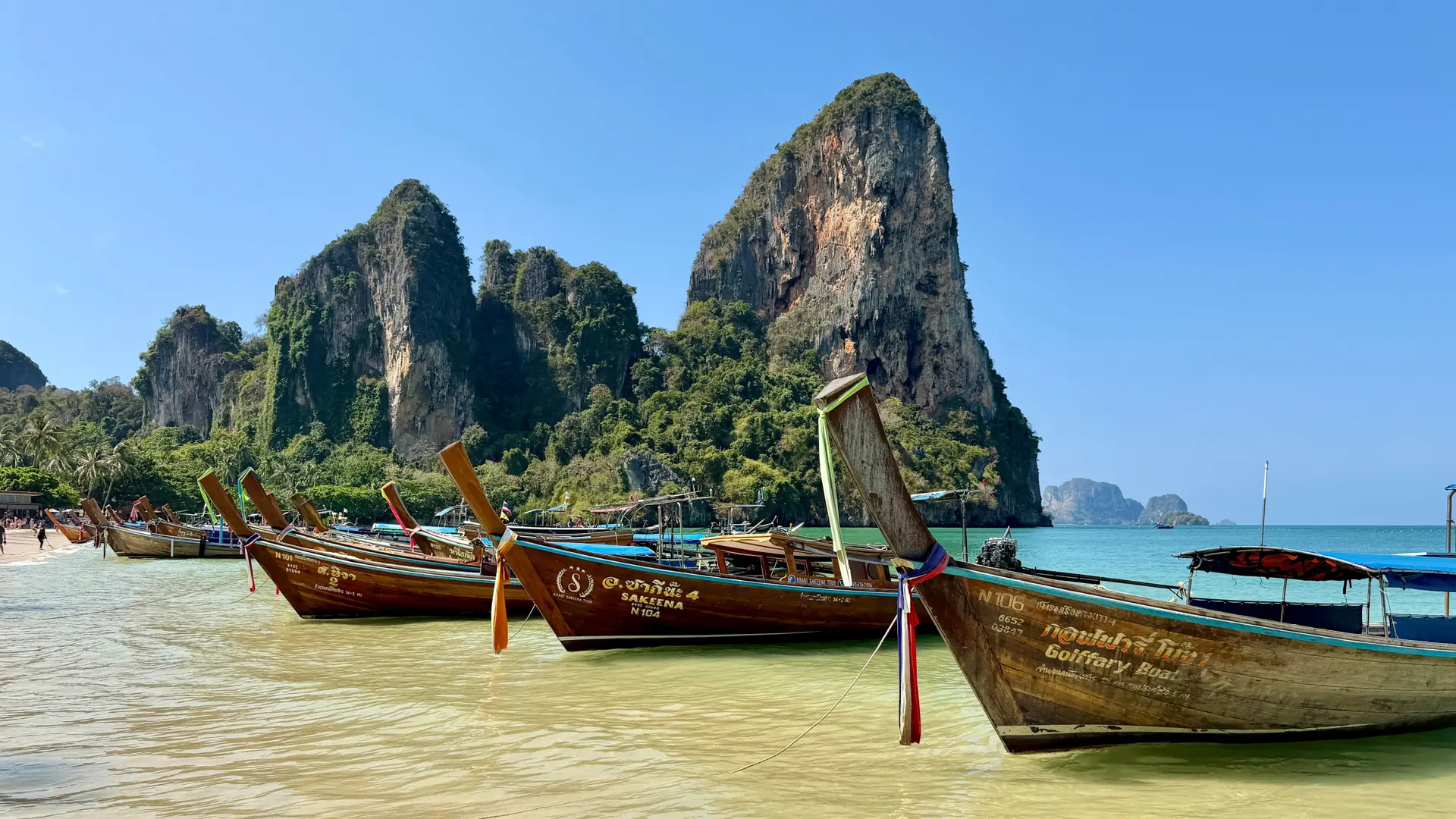 Long-tail boats drawn up on Railay Beach below Krabi's limestone cliffs
