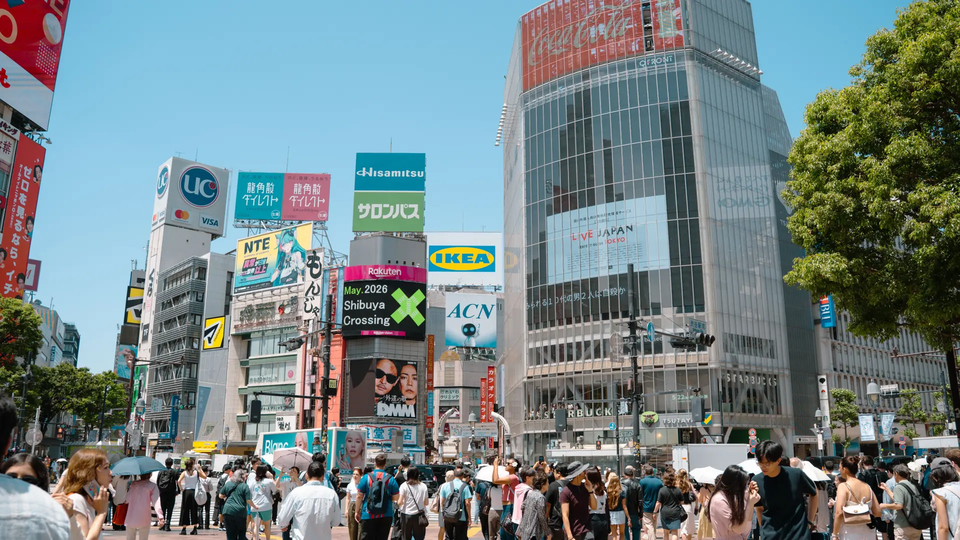 Shibuya Scramble Crossing surrounded by colourful towers in sunny daytime Tokyo