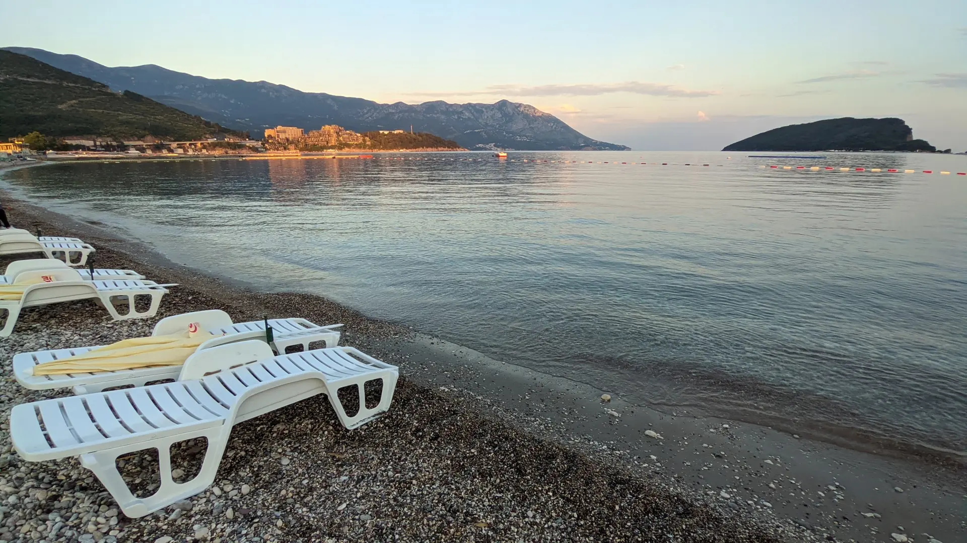 The quiet pebble shore of Slovenska Beach overlooking Budva Bay in daylight