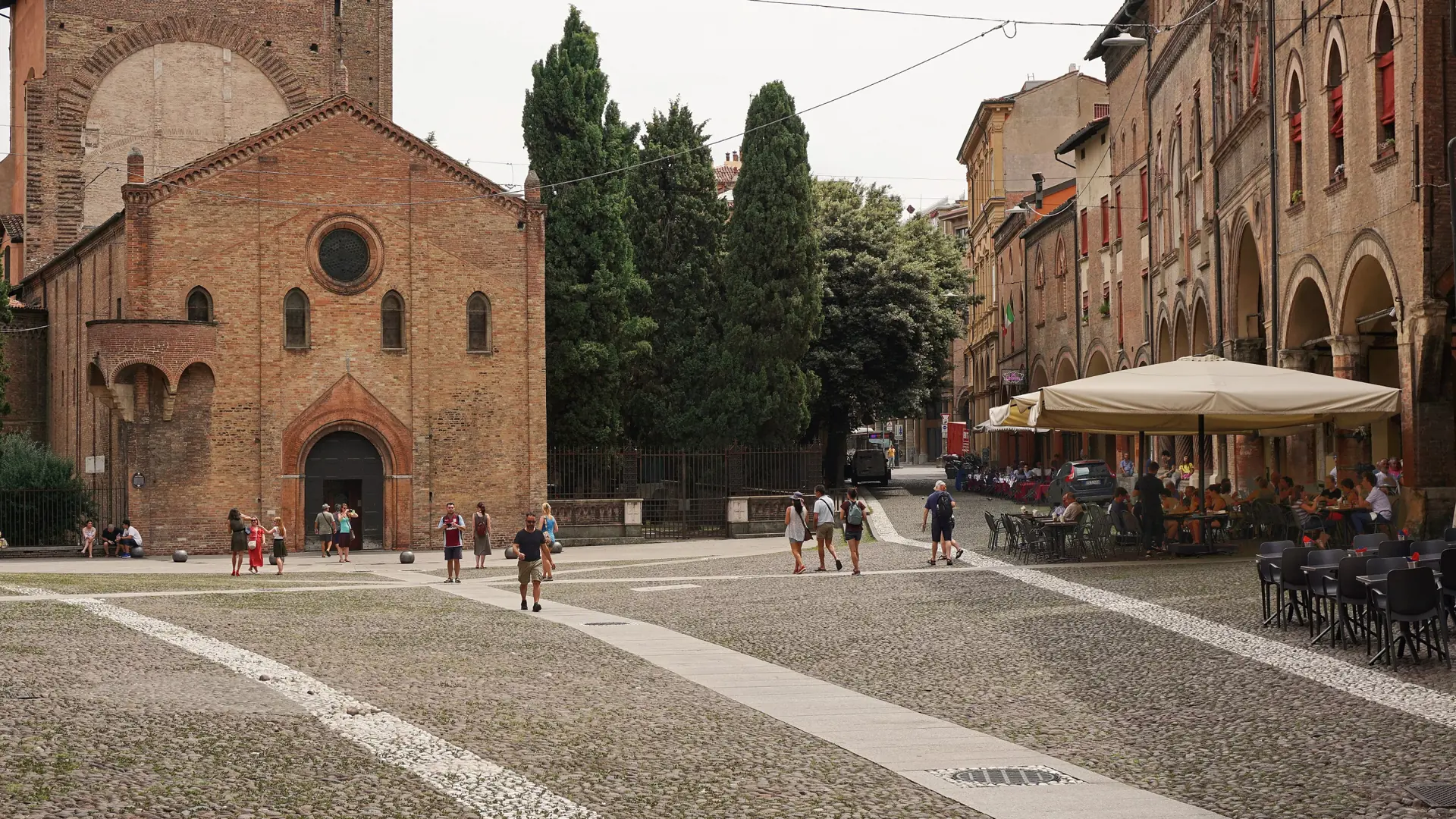 sunlit Piazza Santo Stefano with arcades, historic brick façades and café tables in Bologna