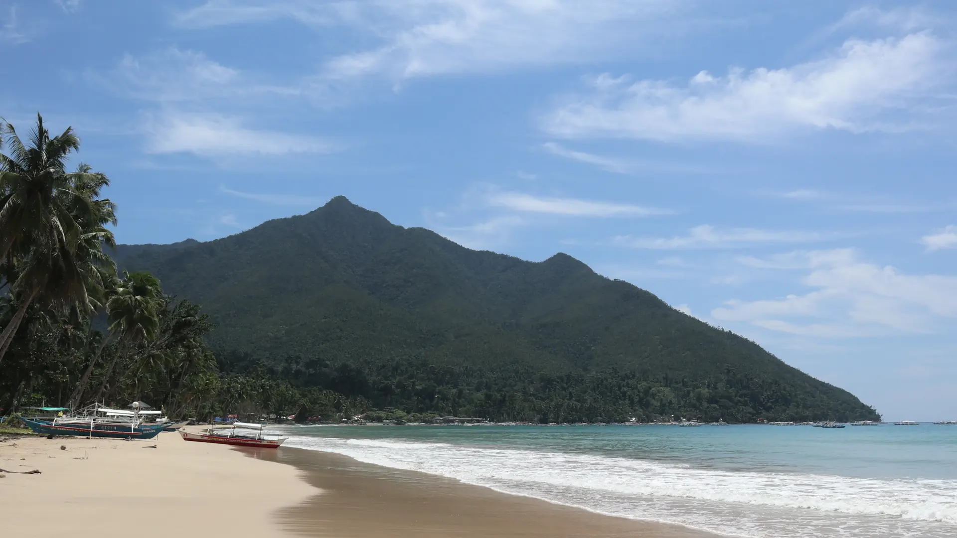 Sabang Beach on Puerto Princesa’s west coast, with pale sand, green palms and blue sea below the hills