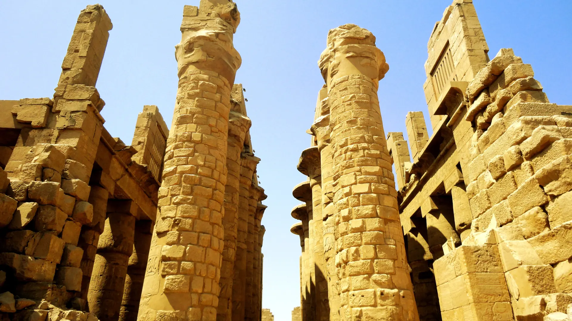 Golden stone columns at Karnak Temple in Luxor under a blue sky.