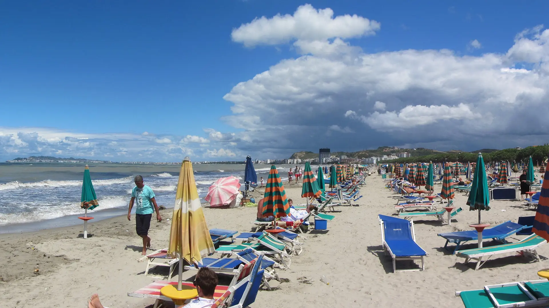 Sunbeds and umbrellas lined up on the wide sandy beach at Golem, south of Durrës, on a sunny day