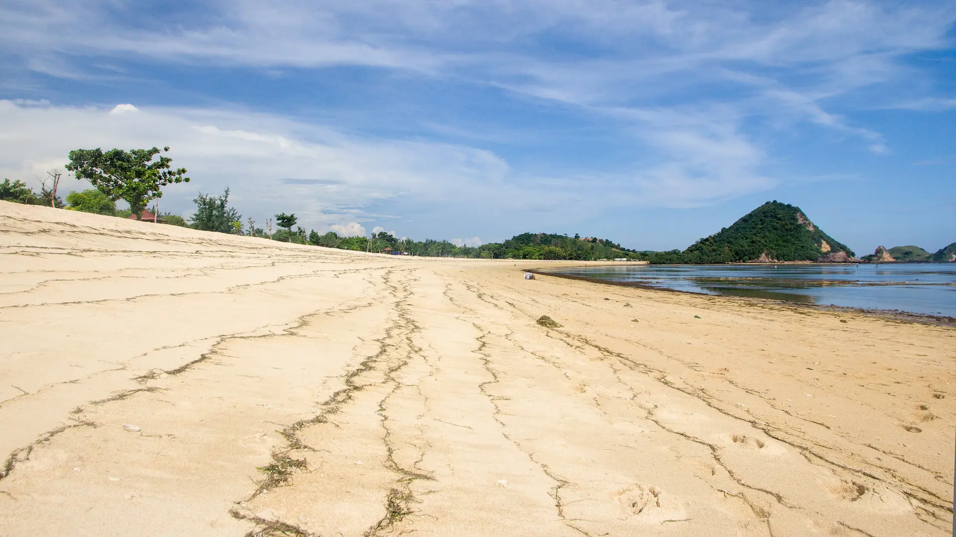 Golden sand and a small green headland at Kuta Beach on Lombok