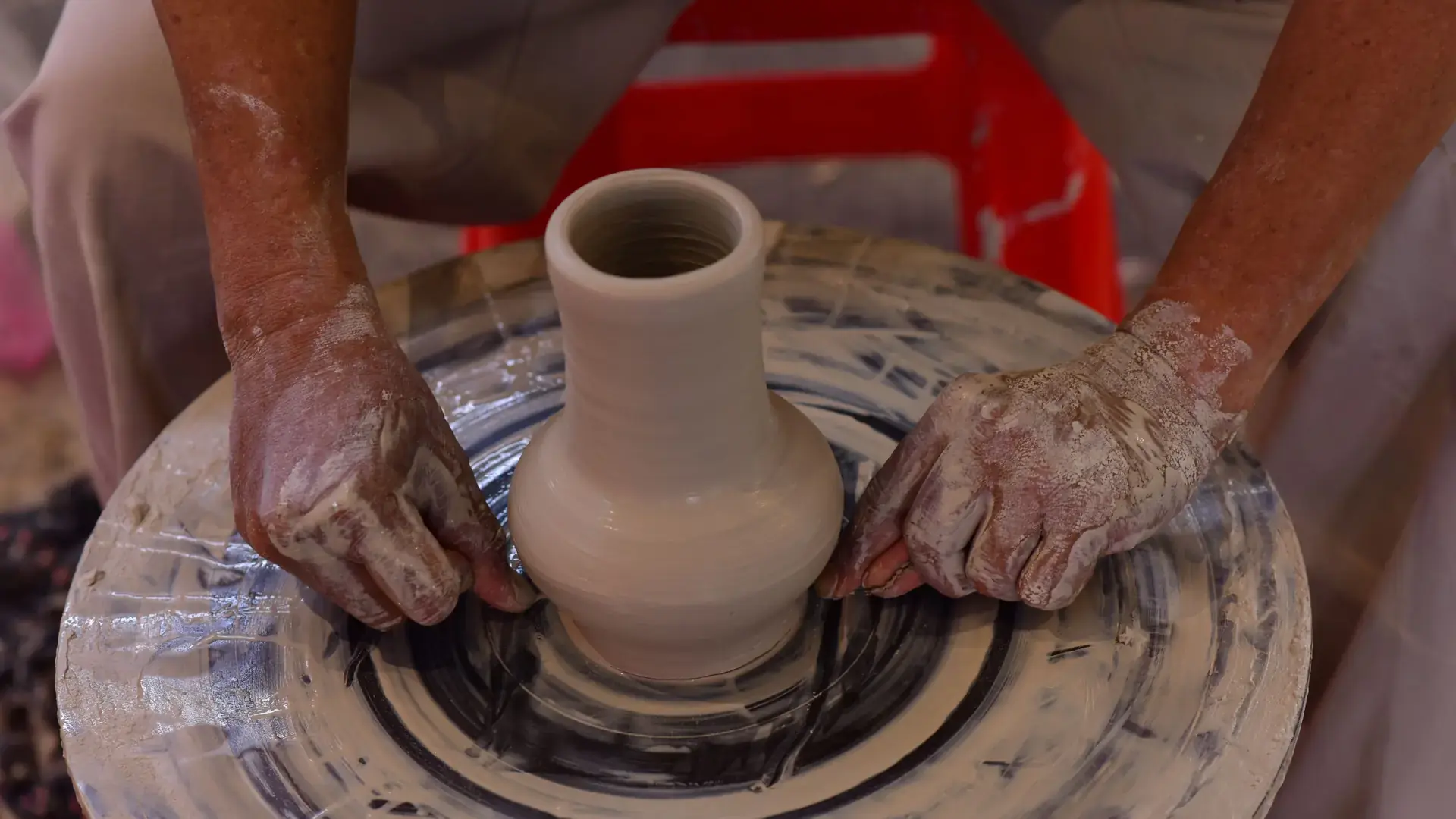 potter shaping a clay vessel by hand on a wheel in a sunlit artisan workshop