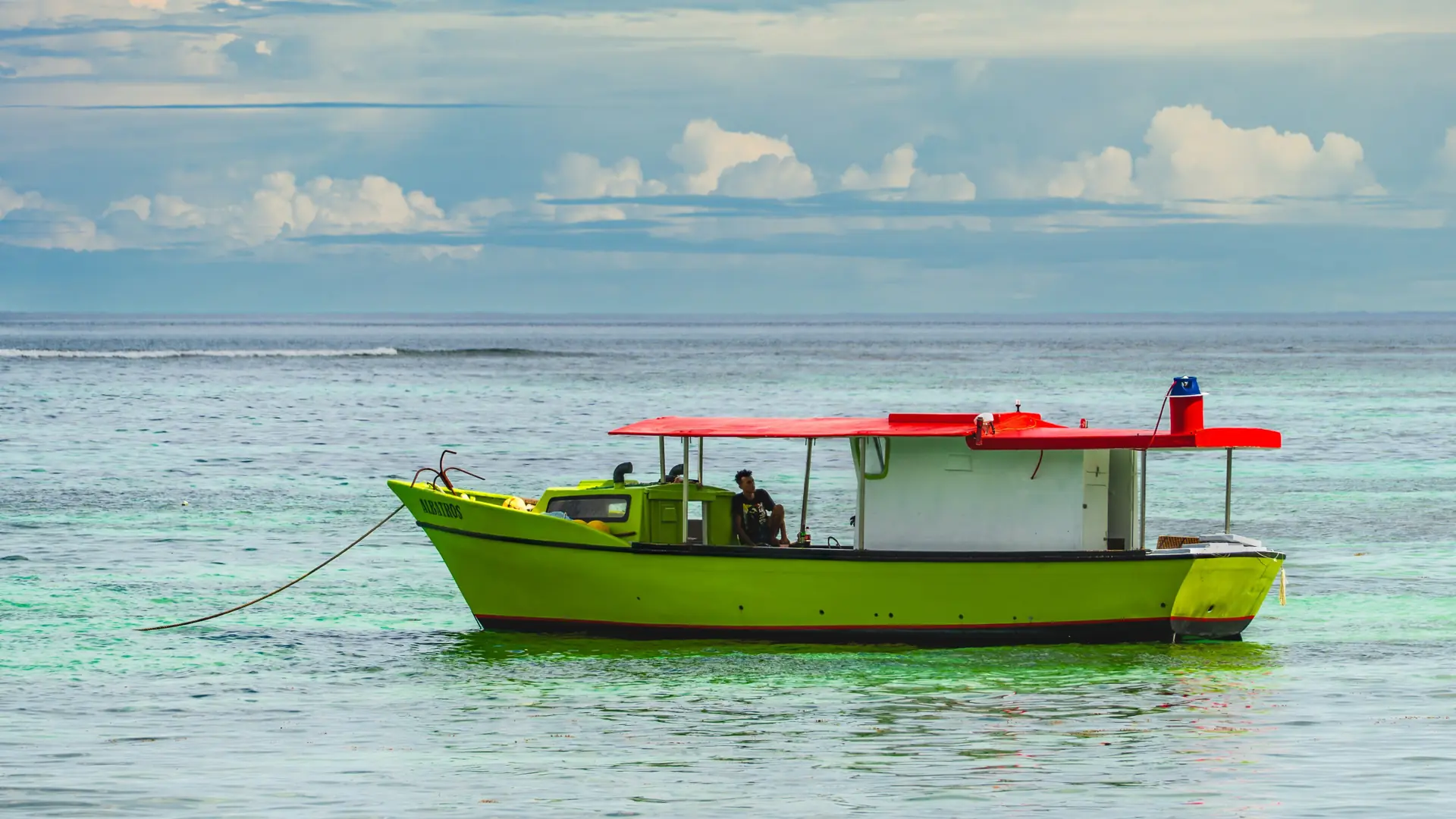 Green fishing boat moored in shallow water at Anse Royale Beach
