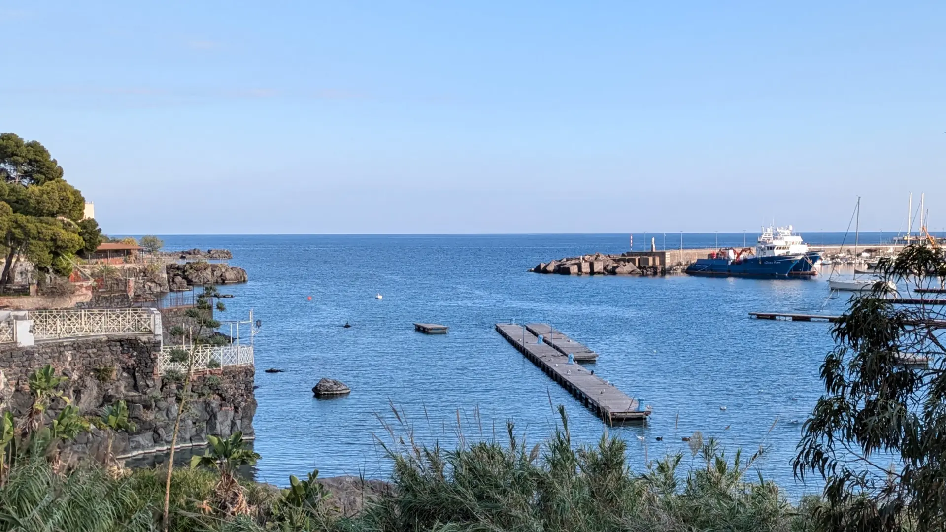 bright Ognina harbour in Catania with fishing boats, blue water and lava-stone waterfront
