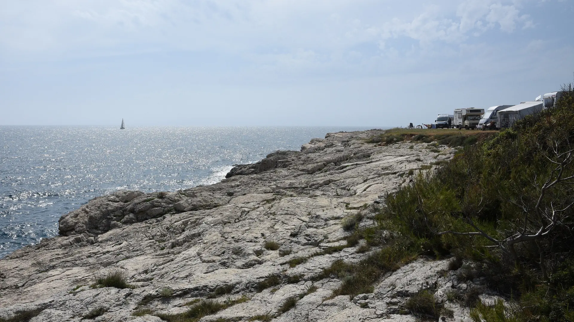 Stoja’s rocky shoreline in Pula, with sunlight on the sea and campers by the coast
