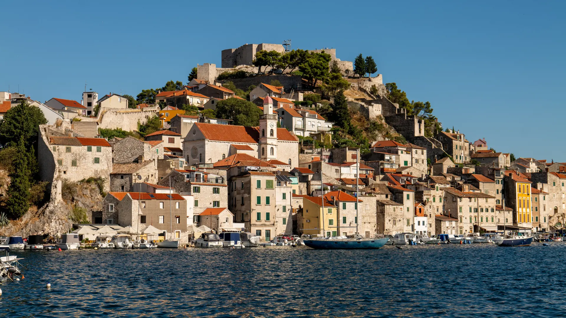 Šibenik’s hillside houses and waterfront below St Michael’s Fortress under a clear blue sky.