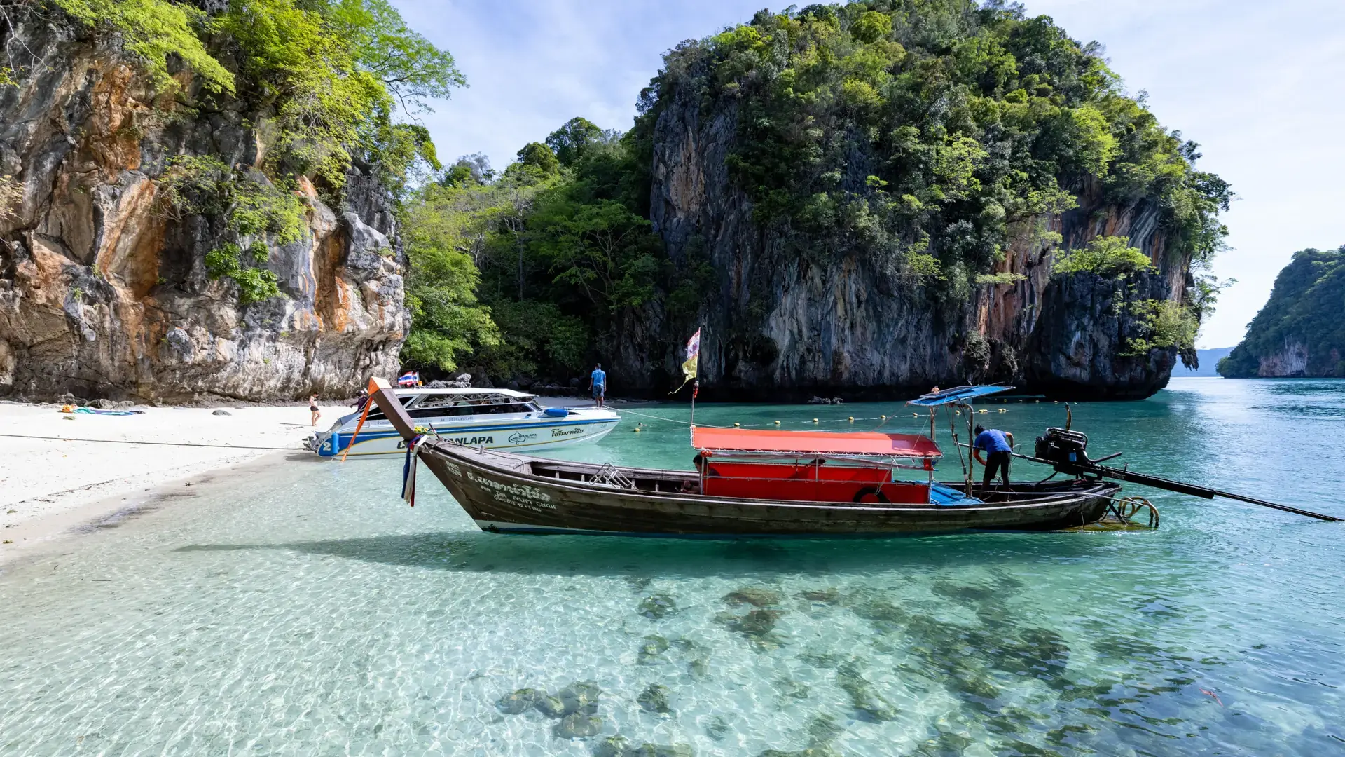 Long-tail boat beside a sunlit Thai limestone island and clear turquoise water