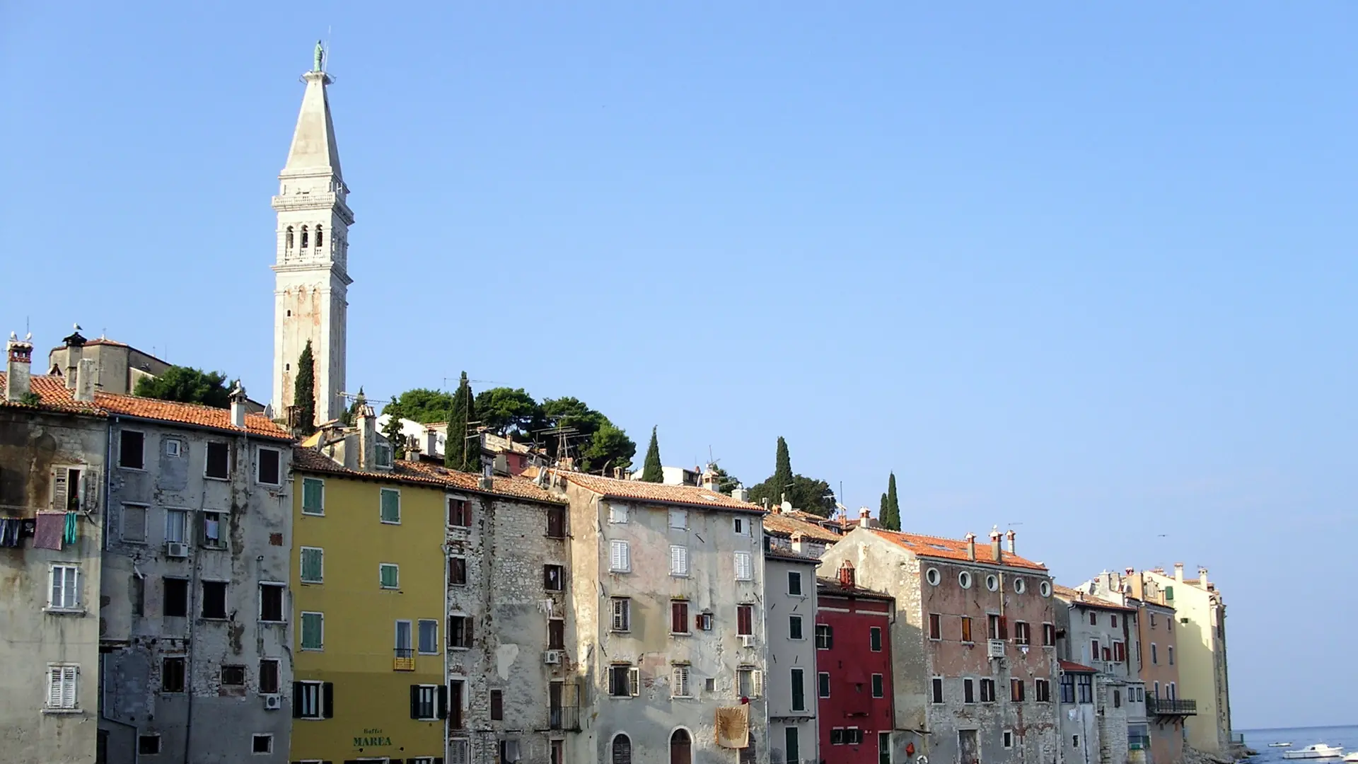 Rovinj's colourful waterfront houses and St Euphemia bell tower under a clear blue sky