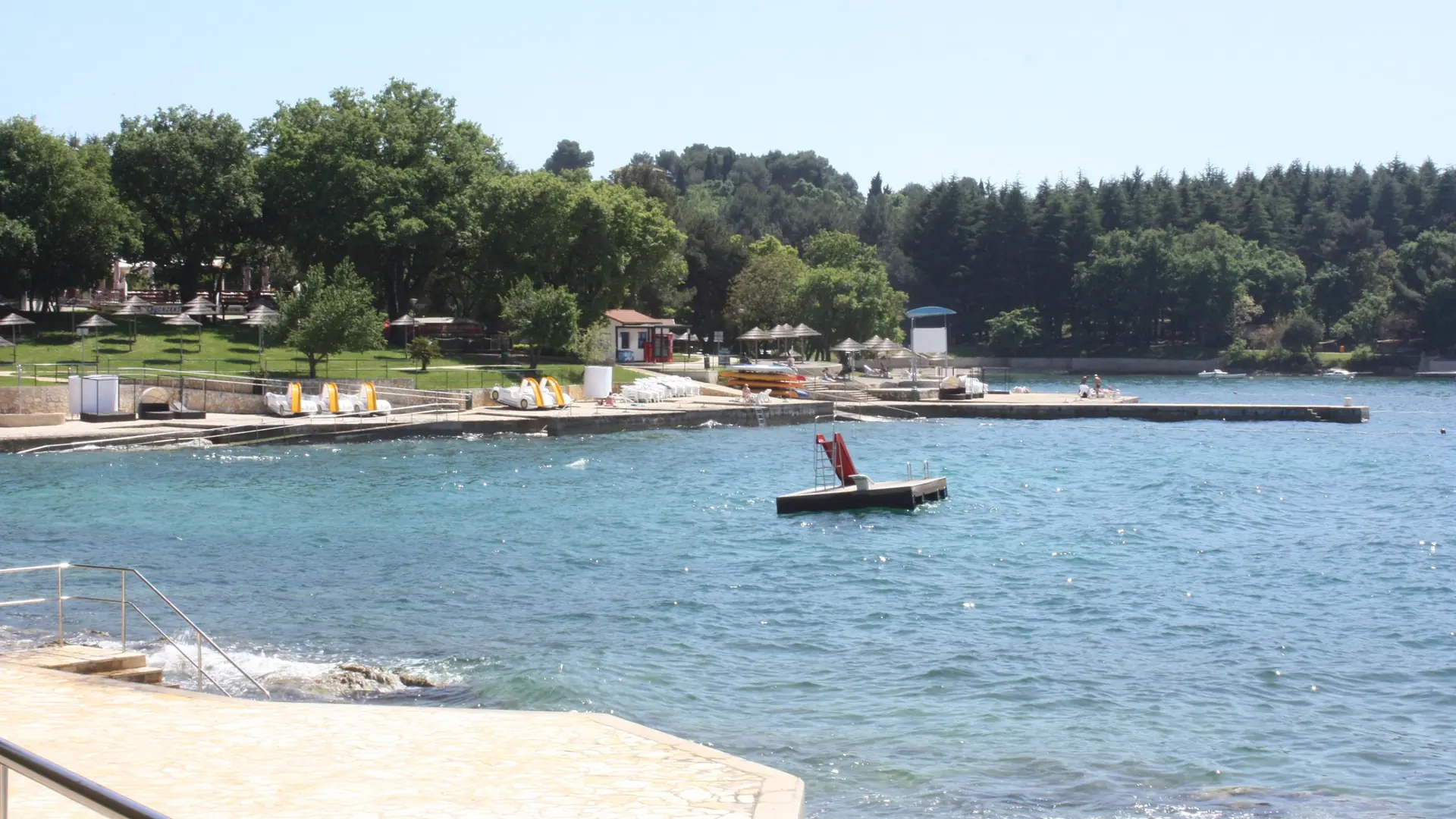 Pine trees, swimming platforms and clear water around U Brula bay in Poreč