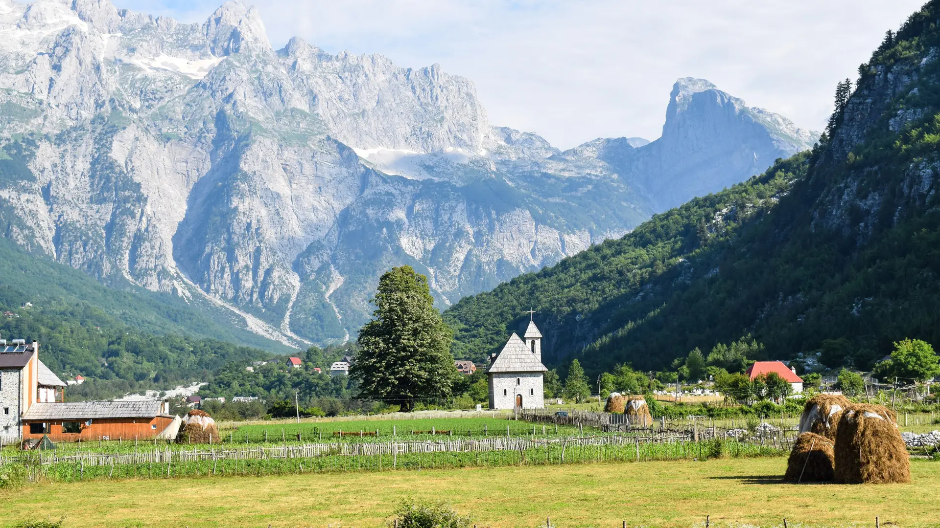 Stone houses and the small church of Theth in a green valley below high peaks on a clear day