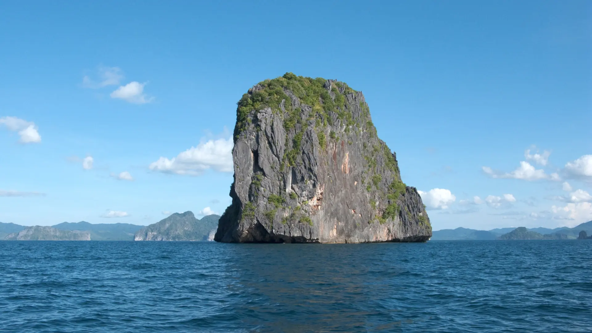 A sunlit limestone island rising from blue water in Bacuit Bay, El Nido