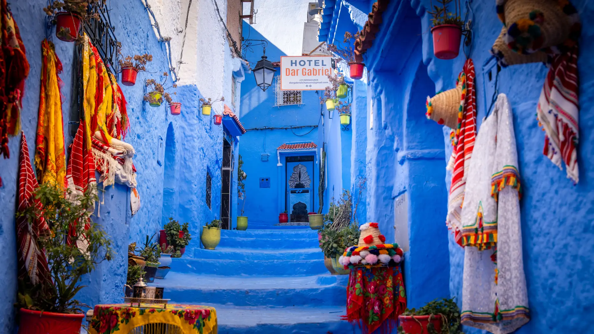 Blue Chefchaouen medina lane with bright textiles and painted steps in daylight