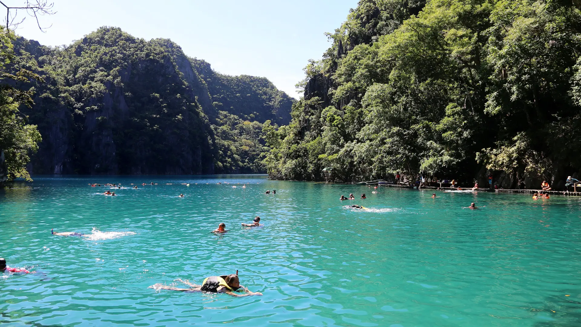 Swimmers in clear turquoise water below limestone cliffs on Coron Island