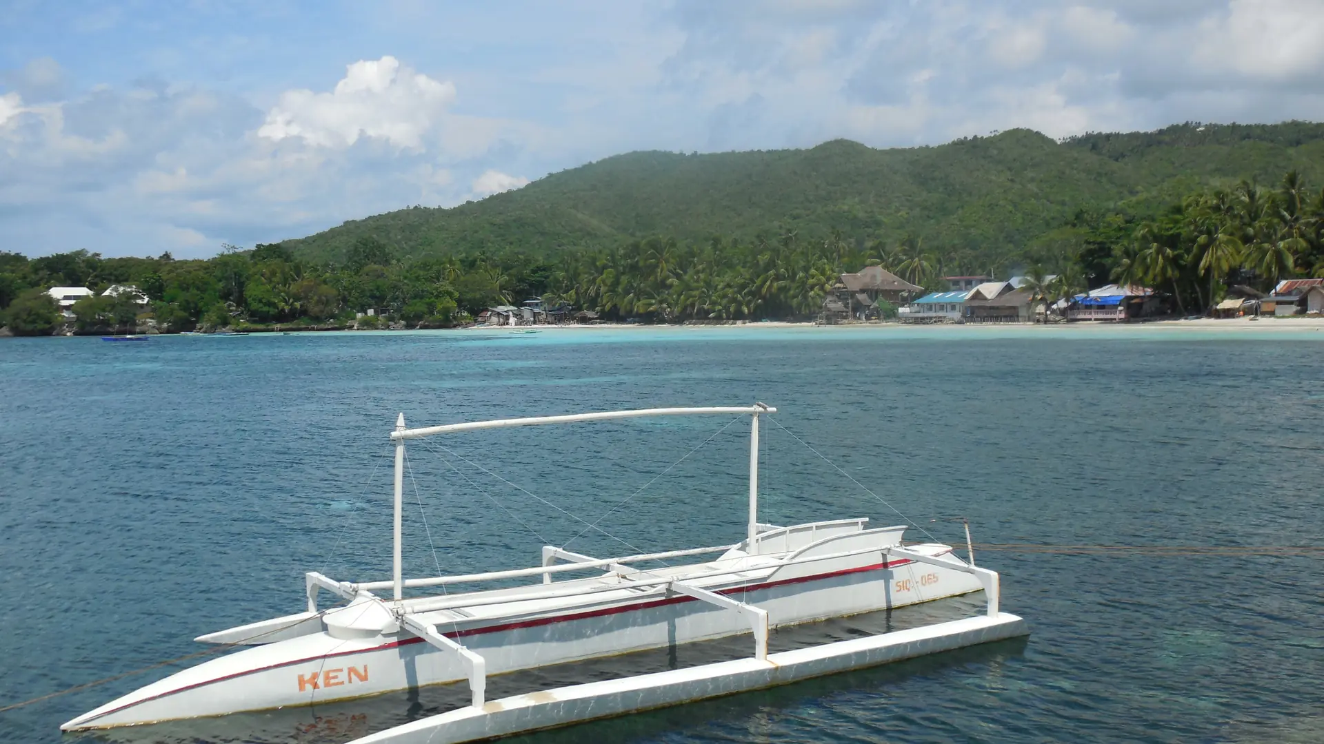 White outrigger boat beside Siquijor’s sandy coastline viewed from the town port