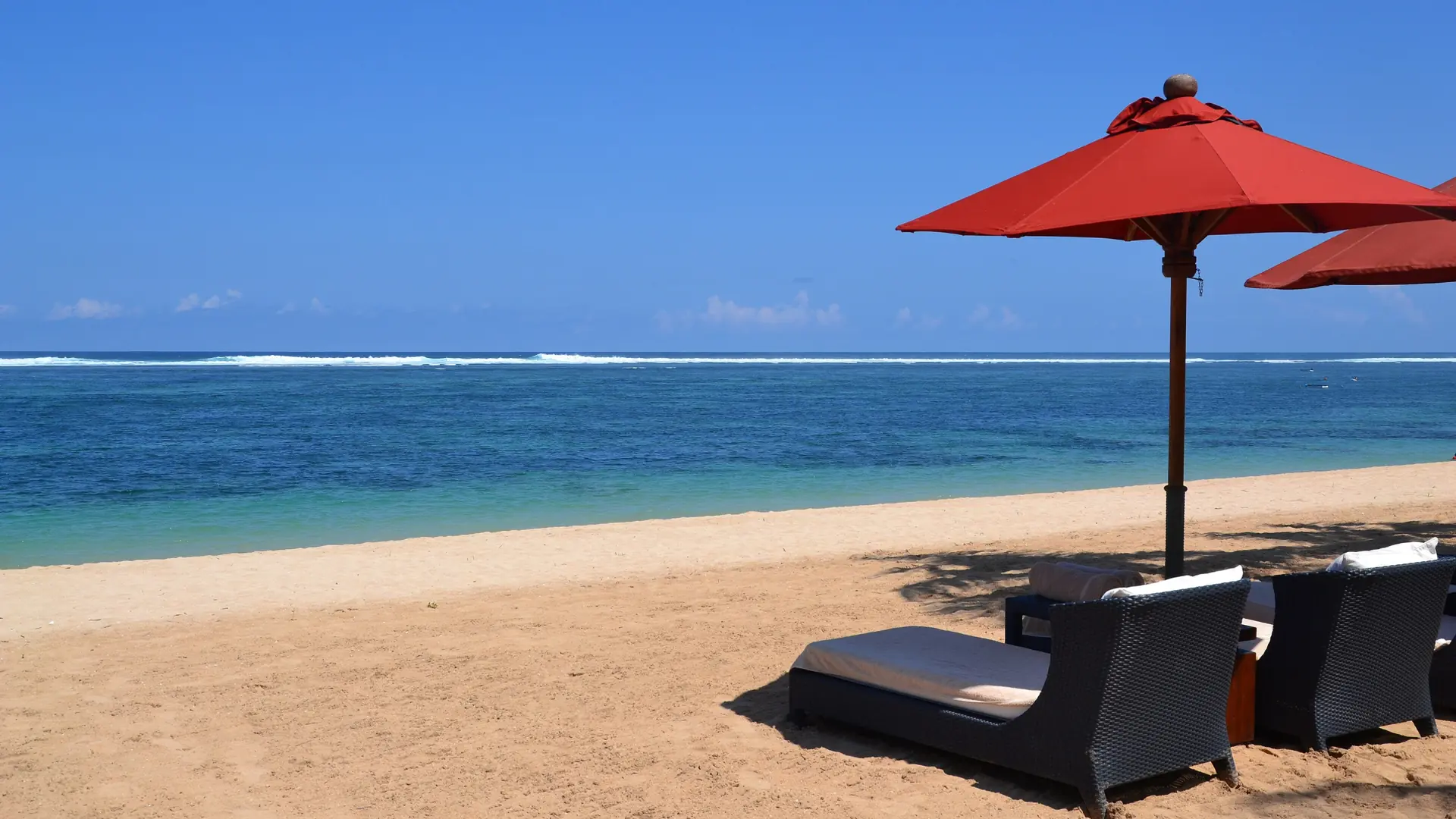 A red parasol and loungers beside bright sand and blue water at St Regis in Nusa Dua