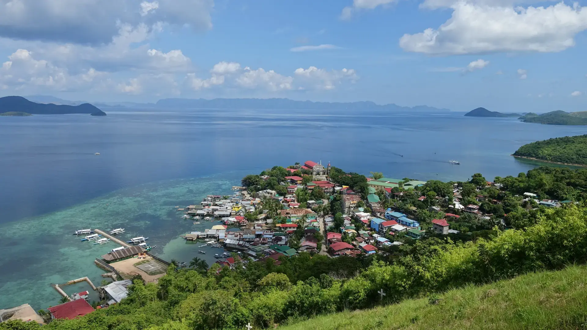 Culion's town of colourful roofs on the water's edge, seen from a green hillside above the bay