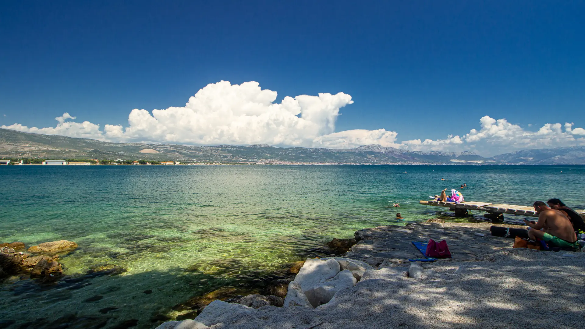 Swimmers beside the rocky shore at Arbanija, looking across the water towards the mainland