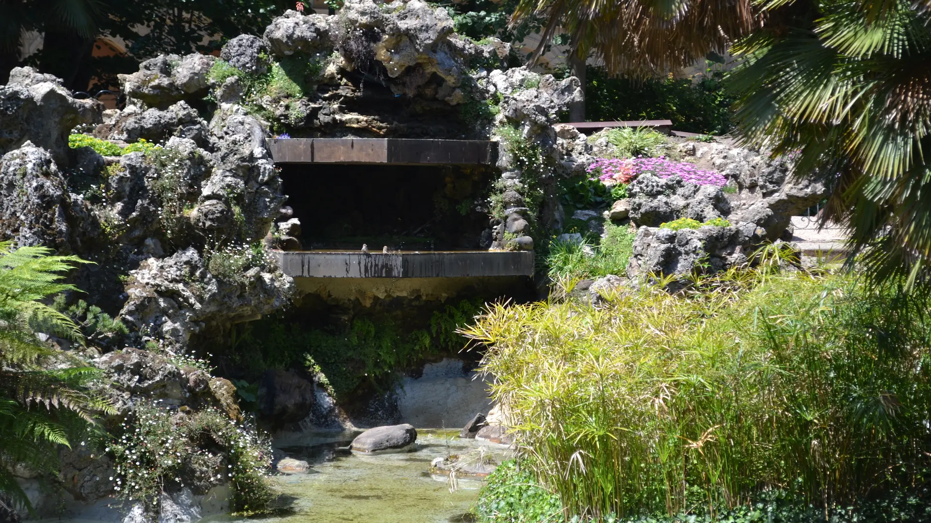 Sunlit plants, a stone cascade and the pond in Plaza Gipuzkoa gardens, Centro, San Sebastián