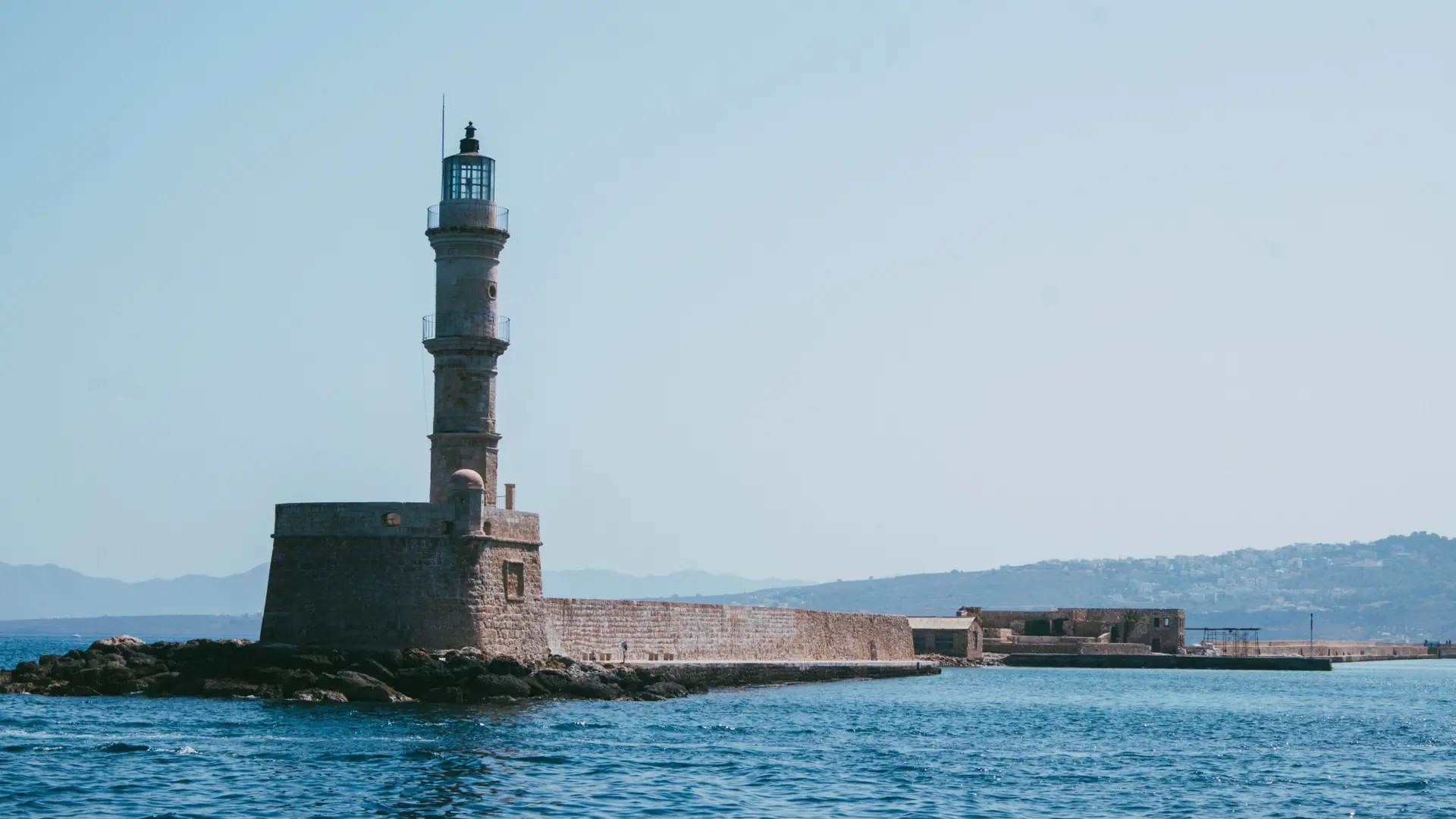 Stone lighthouse at the entrance to Chania's old harbour beside the blue Cretan Sea.