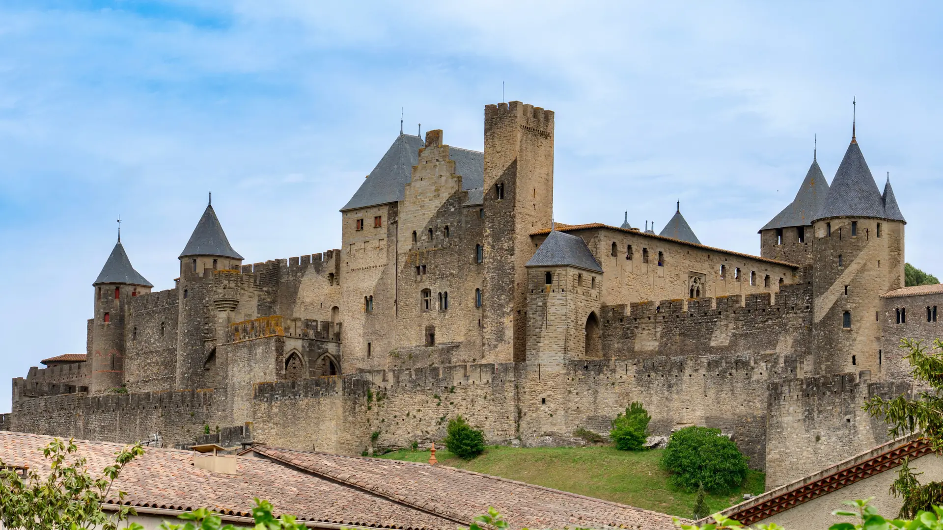 The towers and stone walls of Château Comtal above red-tiled roofs in Carcassonne