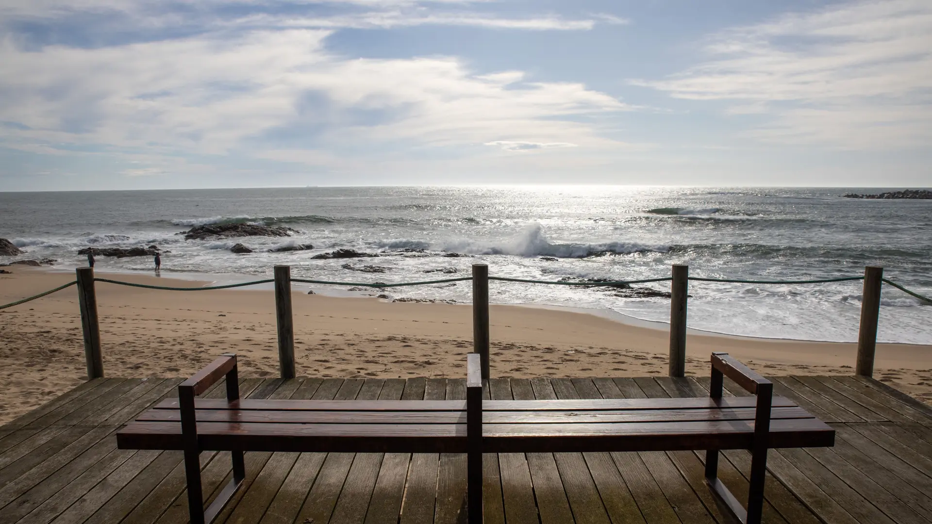 a sunny Atlantic promenade with a wooden bench overlooking waves on the beach