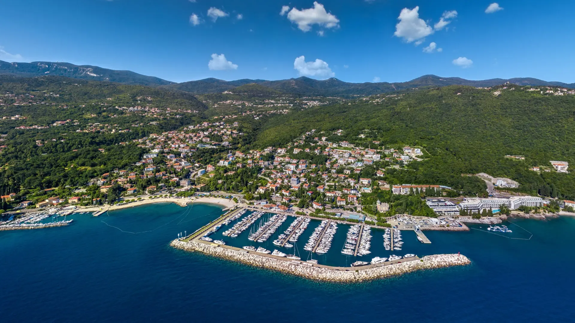 Aerial view of Ičići’s marina, adjacent beach and houses rising into the green hills
