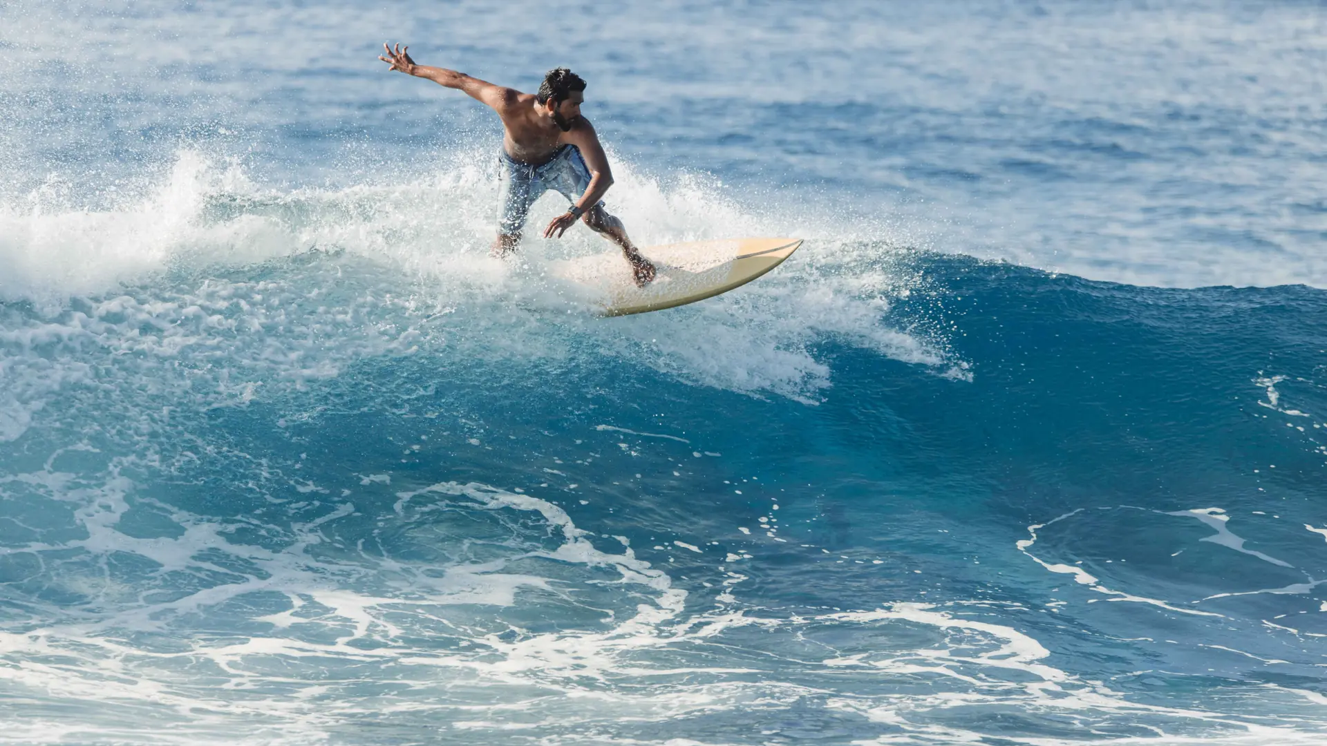 Surfer riding a blue wave in the Maldives in clear daytime light