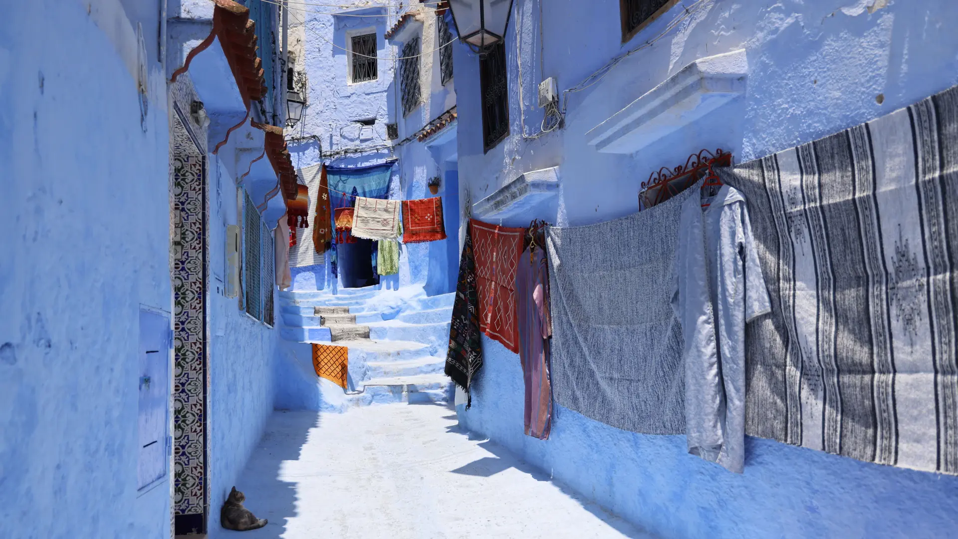 Sunlit blue lane in Chefchaouen with textiles drying above the steps