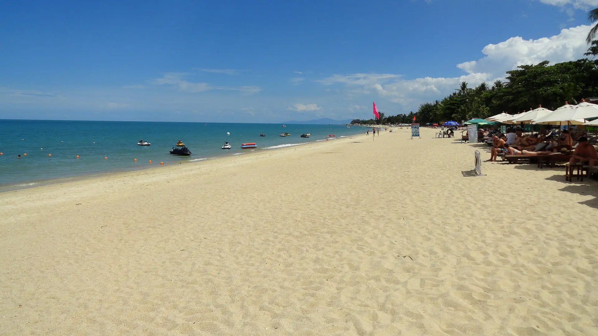 A wide sandy stretch of Lamai Beach with blue sea and beach umbrellas
