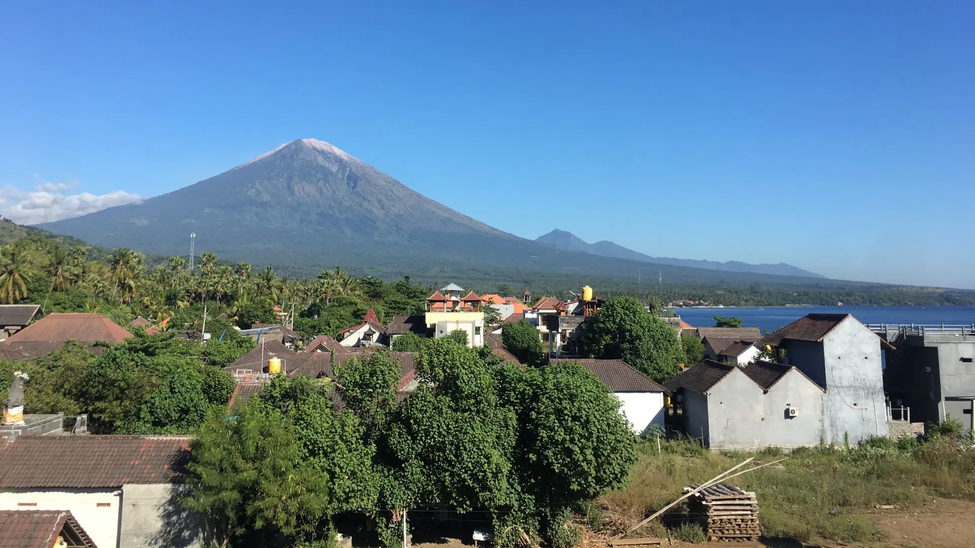 Mount Agung above rooftops and the sea in a wider Amed village view