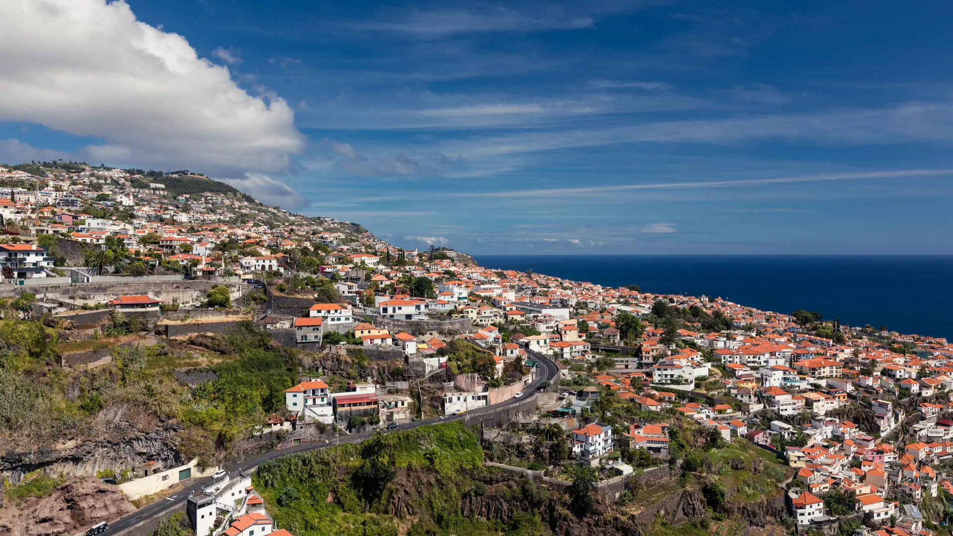 a Madeira hillside town with red-roofed houses cascading toward the sea under a bright blue sky