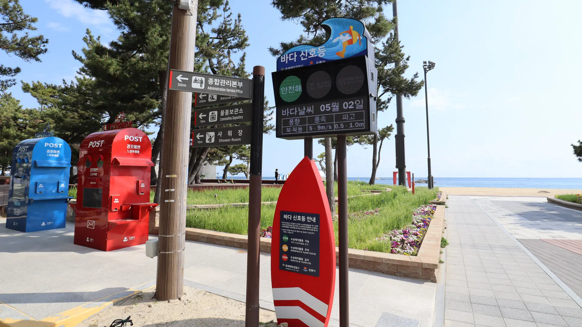Gyeongpo Beach's pine-lined promenade with a '경포해변' (Gyeongpo Beach) signpost, under a bright blue sky, Gangneung