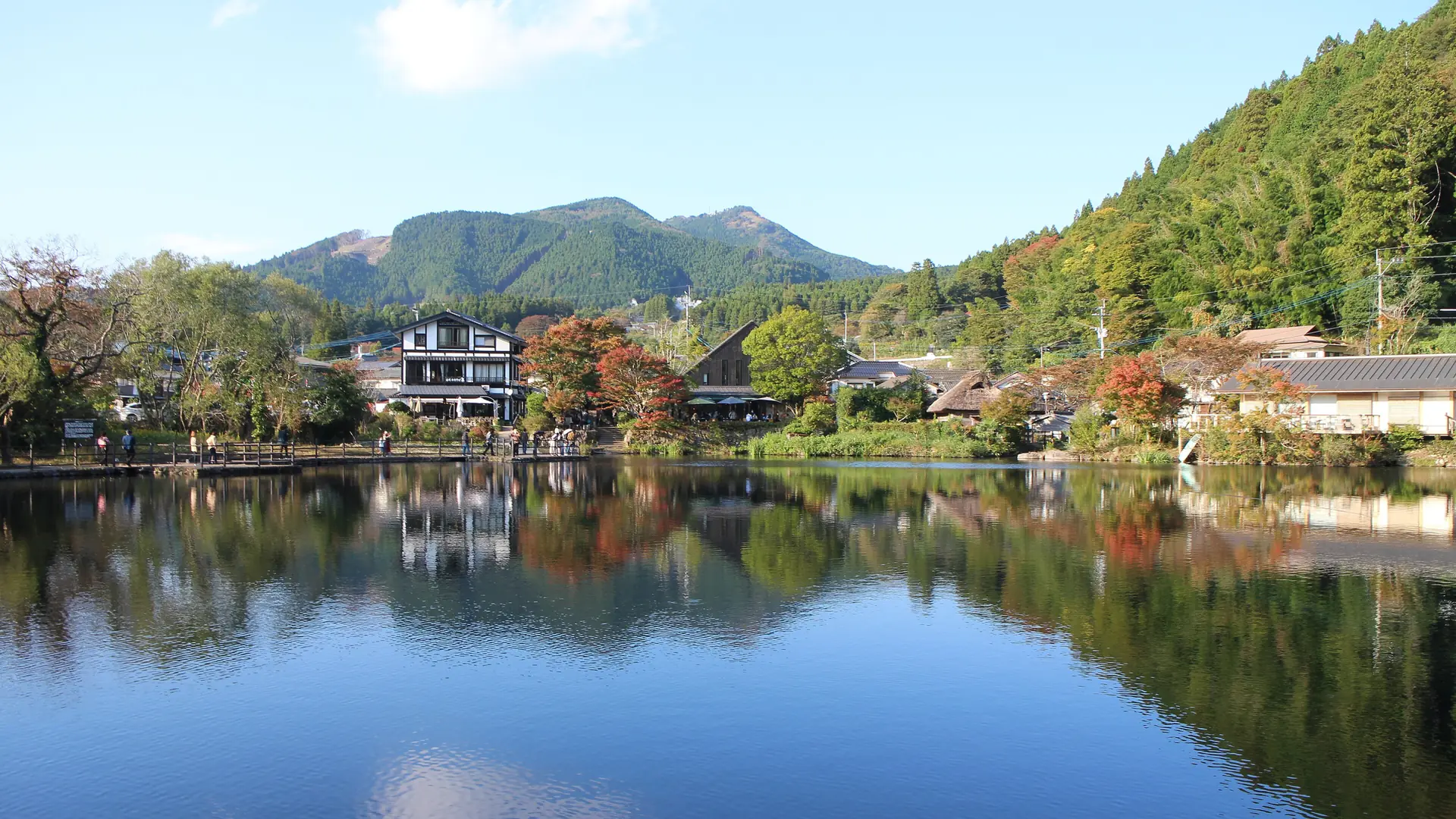 Sunlit trees and lakeside buildings reflected in Lake Kinrin in Yufuin.