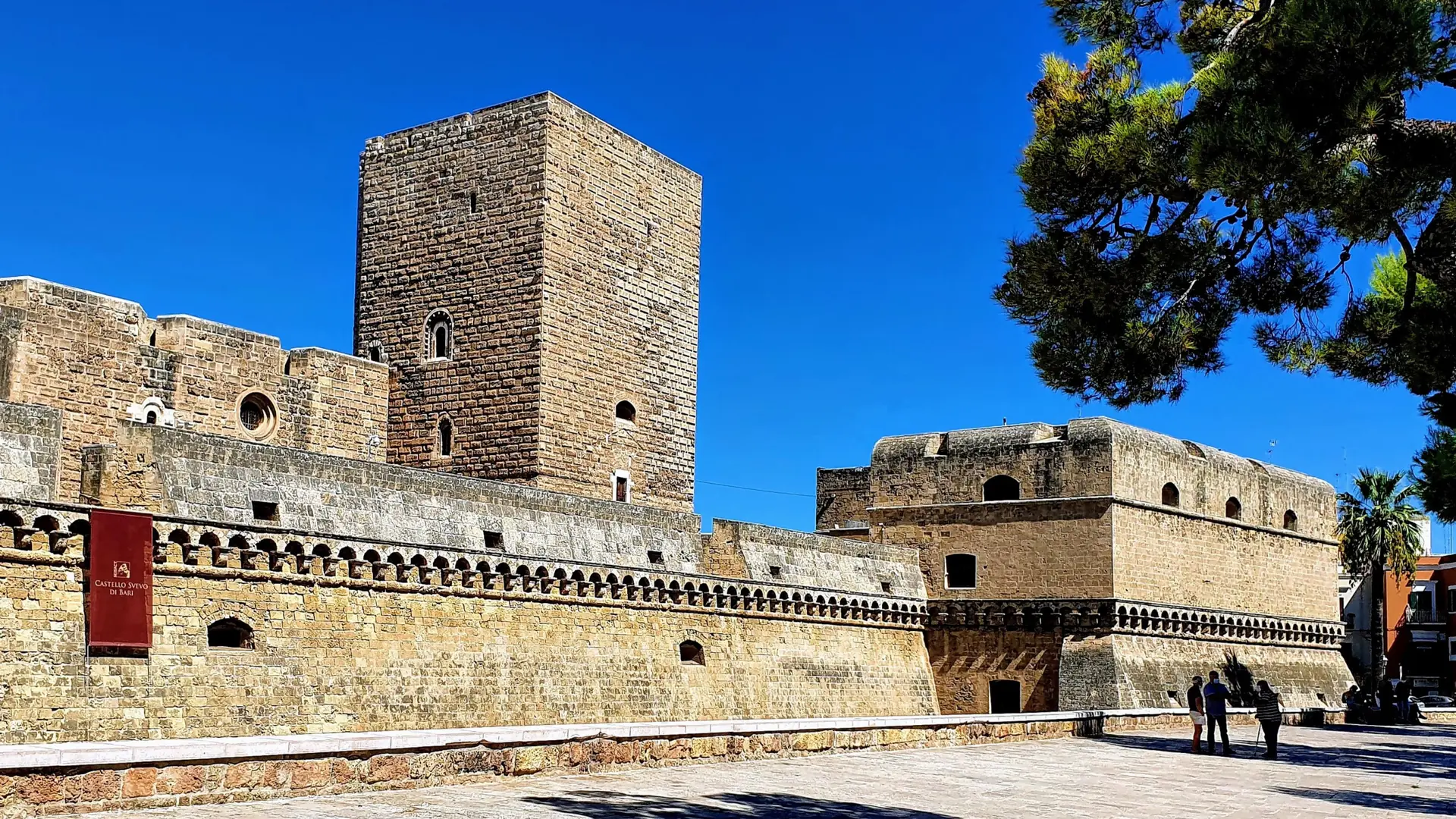 Castello Svevo's stone tower and ramparts under a clear blue sky in Bari