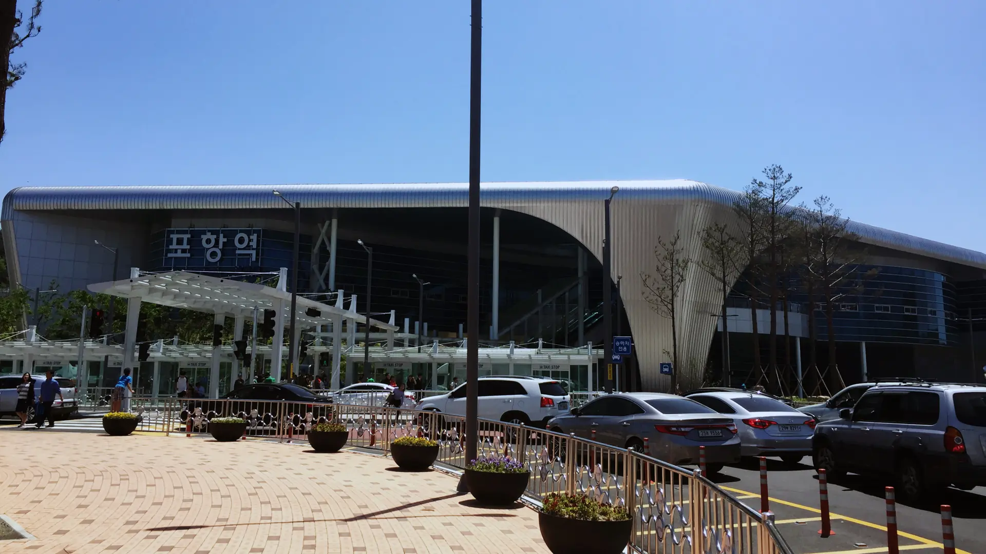 Pohang Station's curved modern terminal building with its large '포항역' (Pohang Station) sign, under a bright blue sky