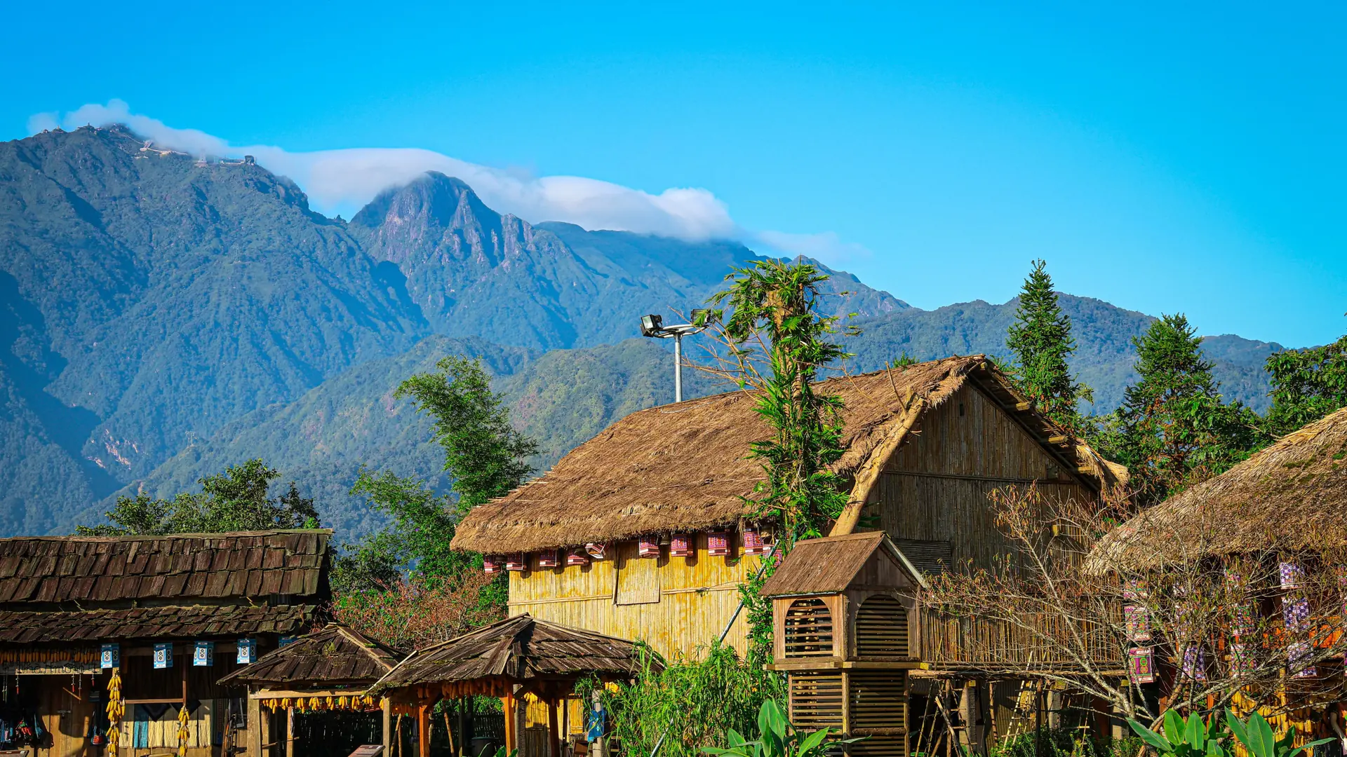 Thatched wooden buildings beneath mountains in the wider Sapa region