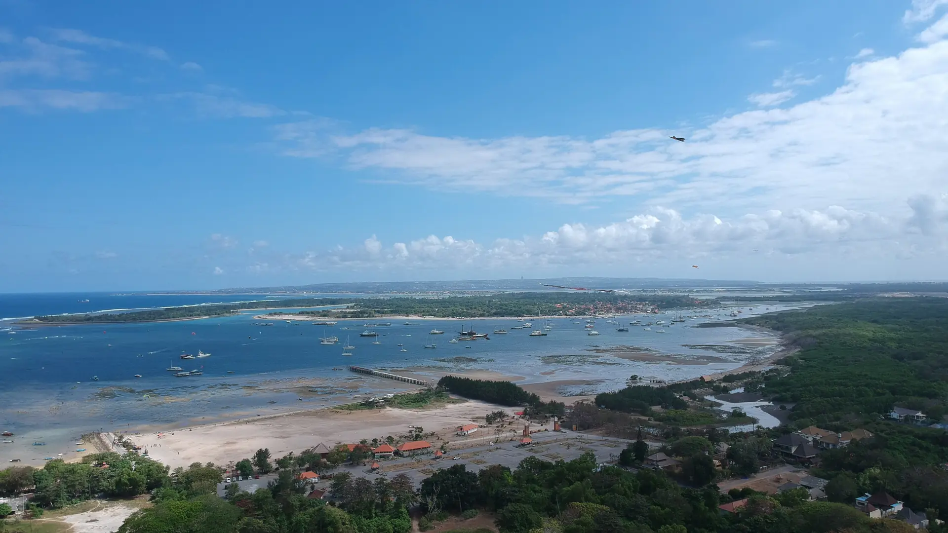 Aerial view of Mertasari beach, blue coastal water and the green shoreline toward Serangan island in Bali
