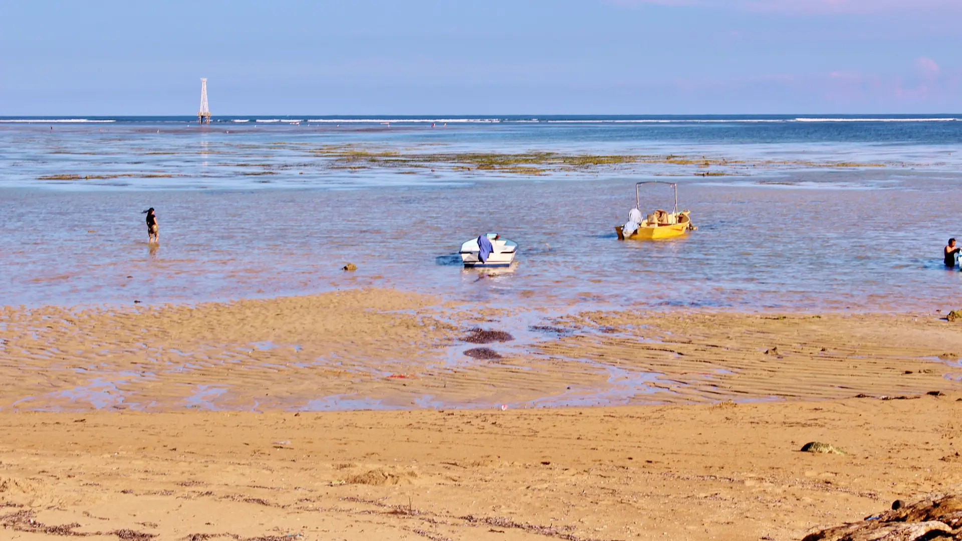 Yellow and white boats in shallow blue water beside the sandy shore in southern Sanur