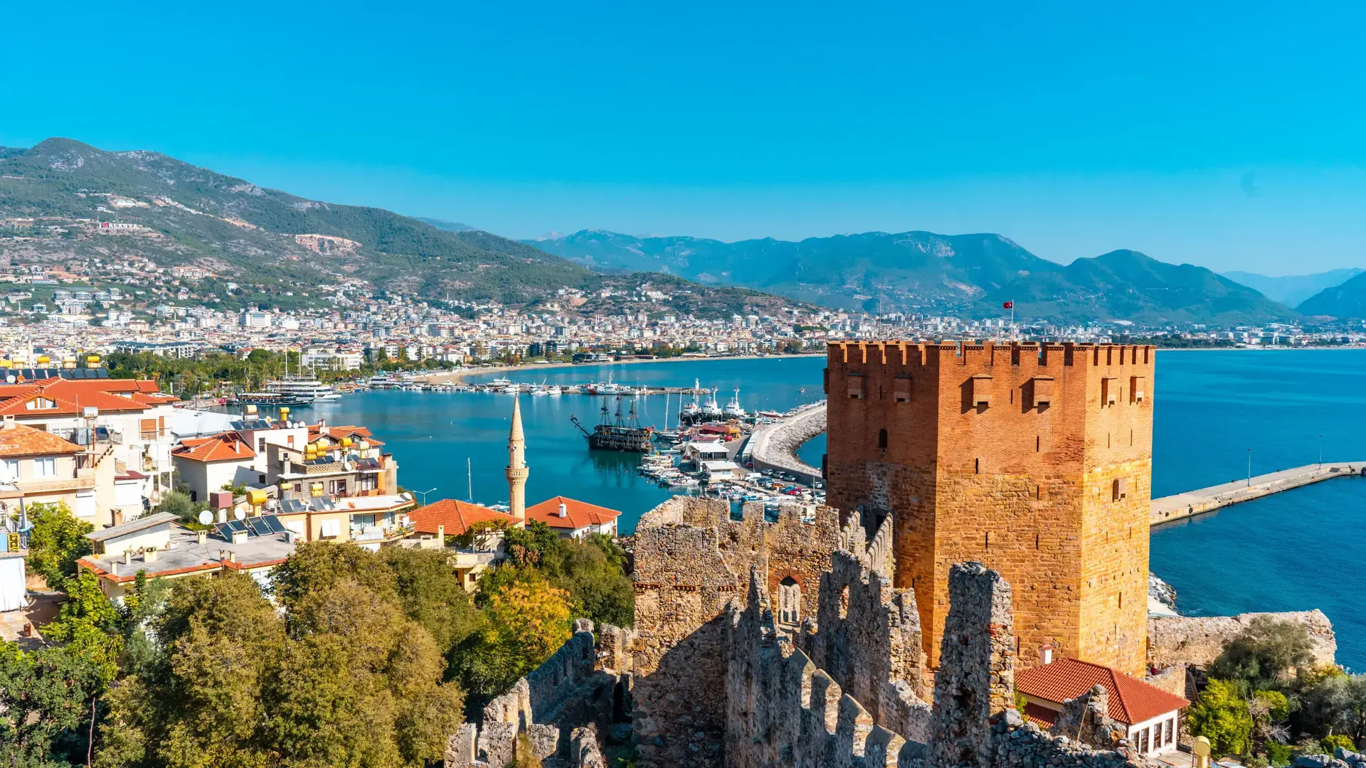 Alanya Red Tower and harbour boats beneath the sunlit castle peninsula