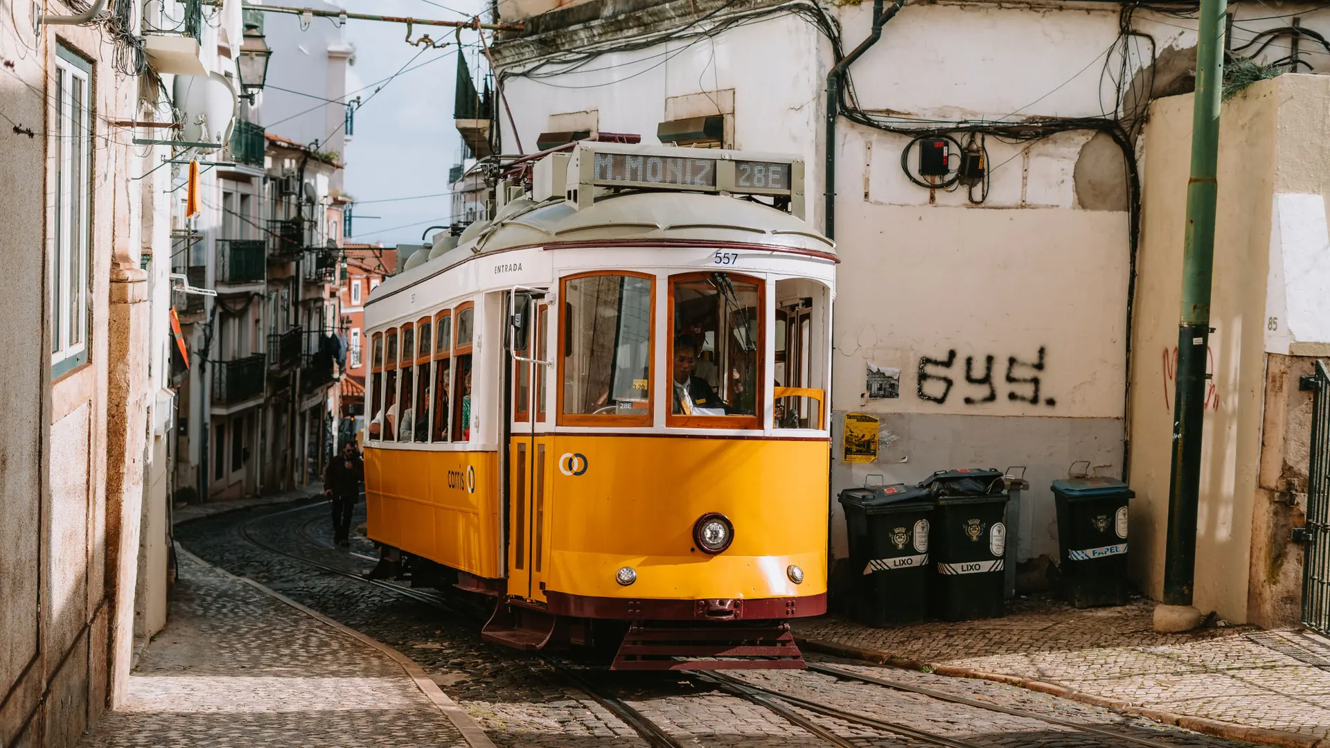 Yellow Lisbon tram climbing past tiled facades in bright morning light