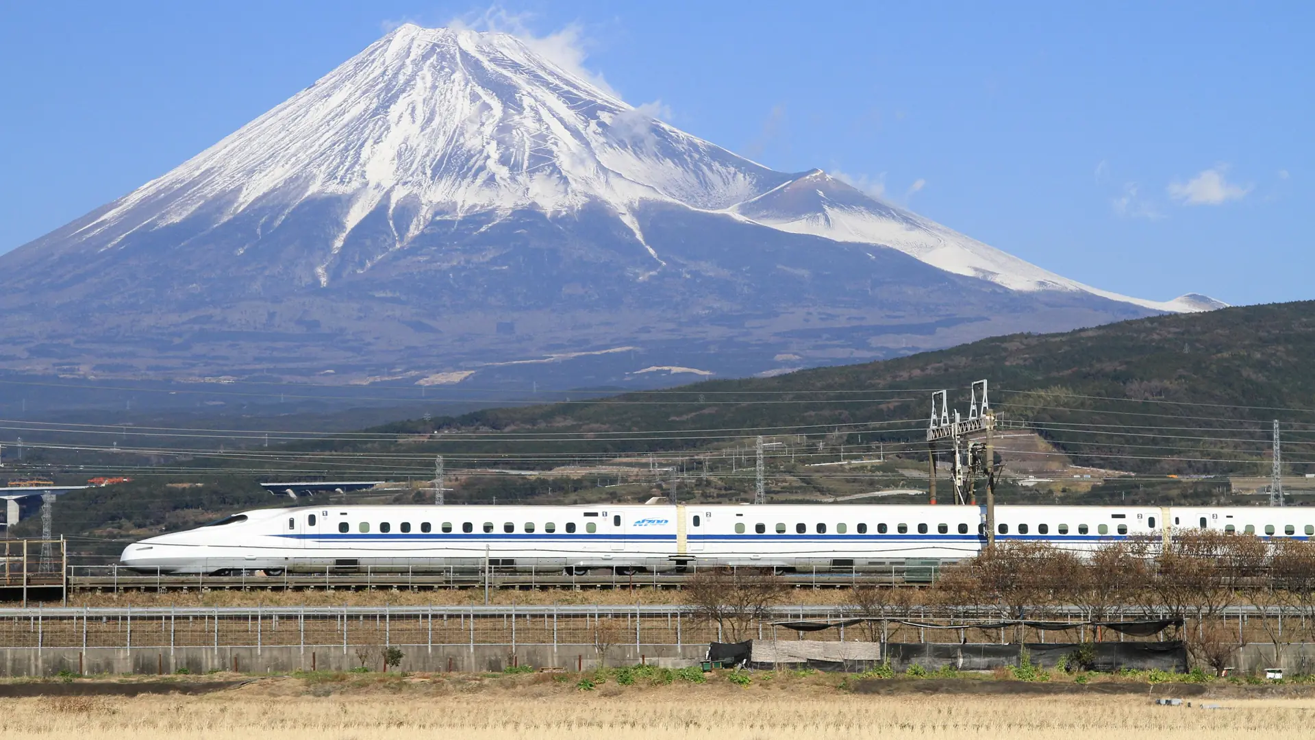 A white shinkansen passing Mount Fuji through a bright Japanese landscape