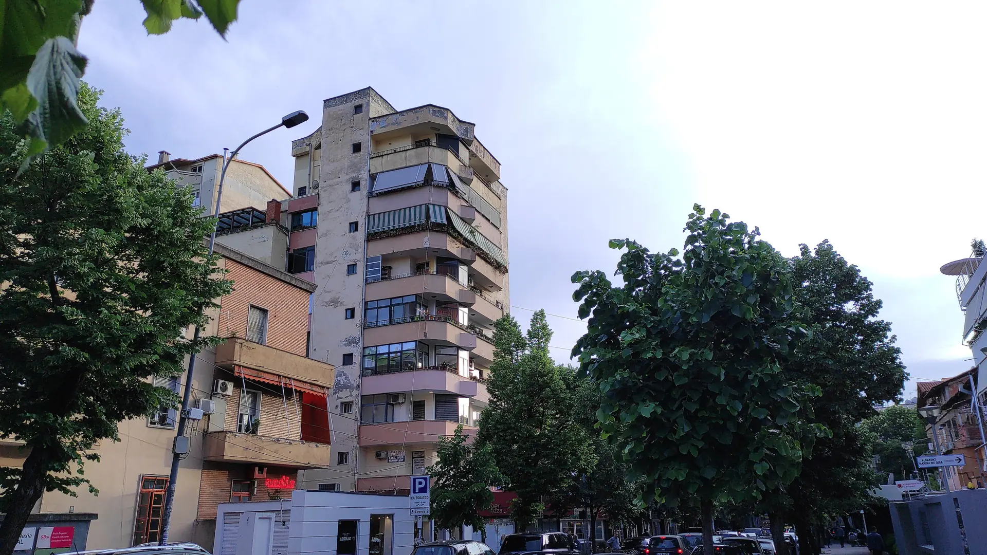 Apartment blocks and leafy trees along a sunny street in Tirana's Blloku district