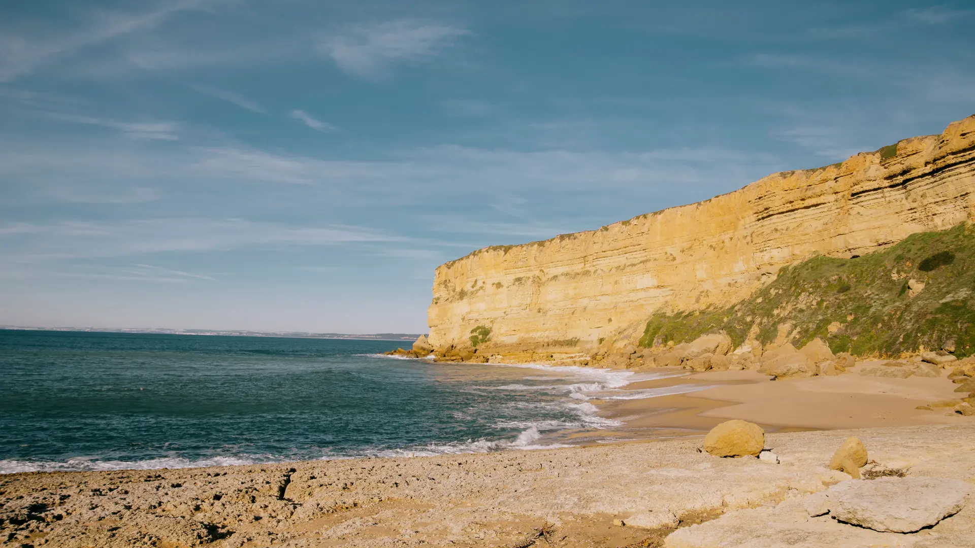 a sandy cove beneath golden limestone cliffs near Lagos under a clear blue sky