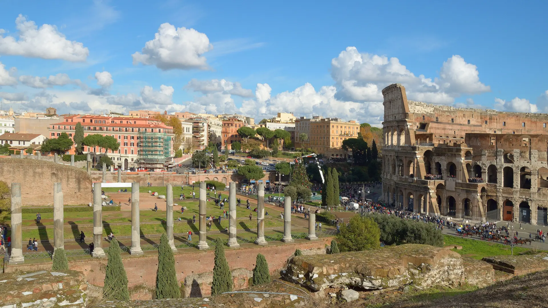 The Colosseum rising beyond the Roman Forum's ancient columns under a bright blue sky