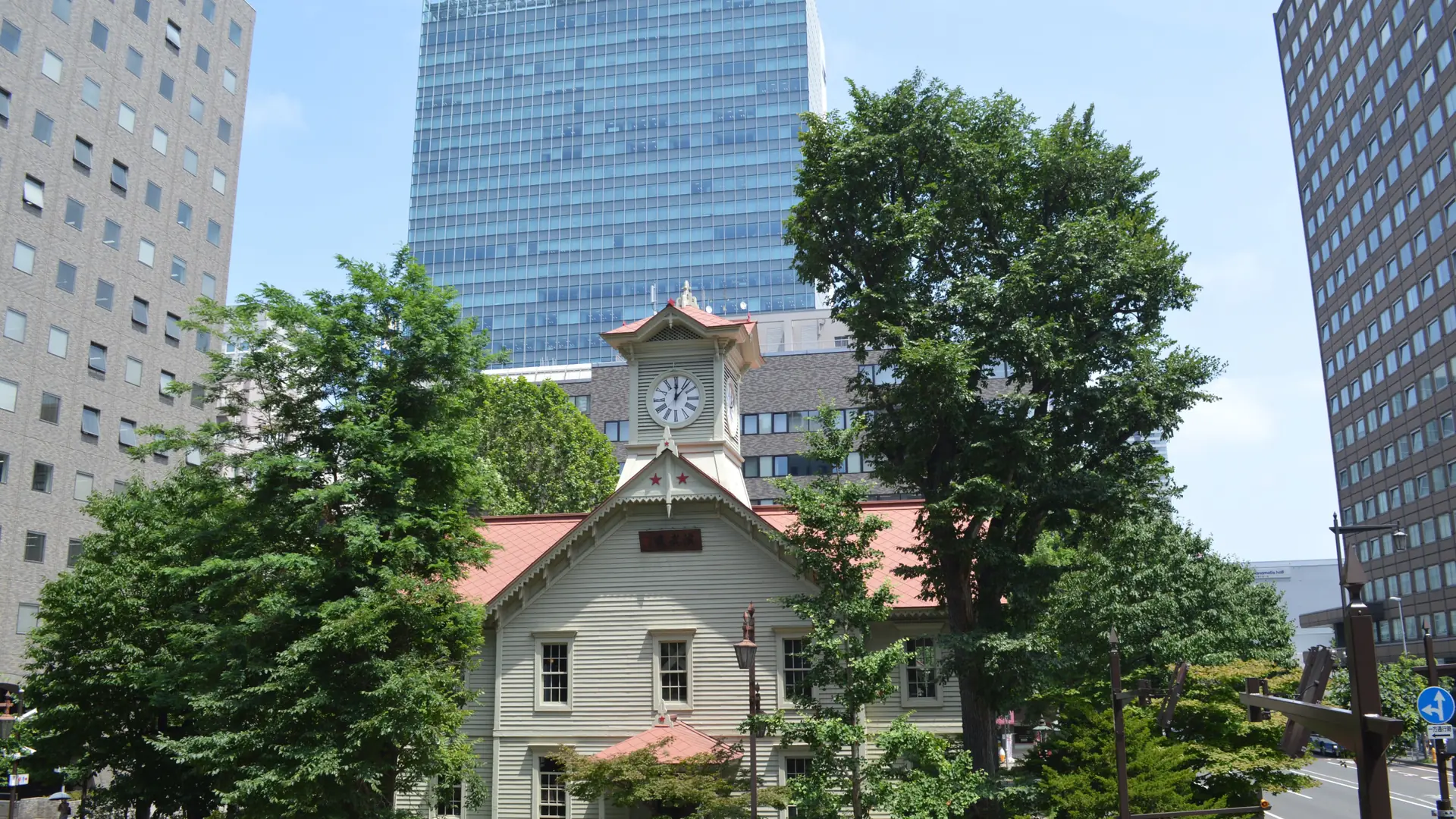 Sapporo Clock Tower framed by green trees and modern city buildings in daylight