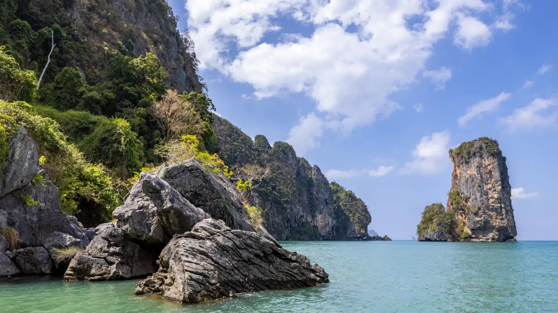 Limestone cliffs and a freestanding karst beside clear shallows on Krabi's coast
