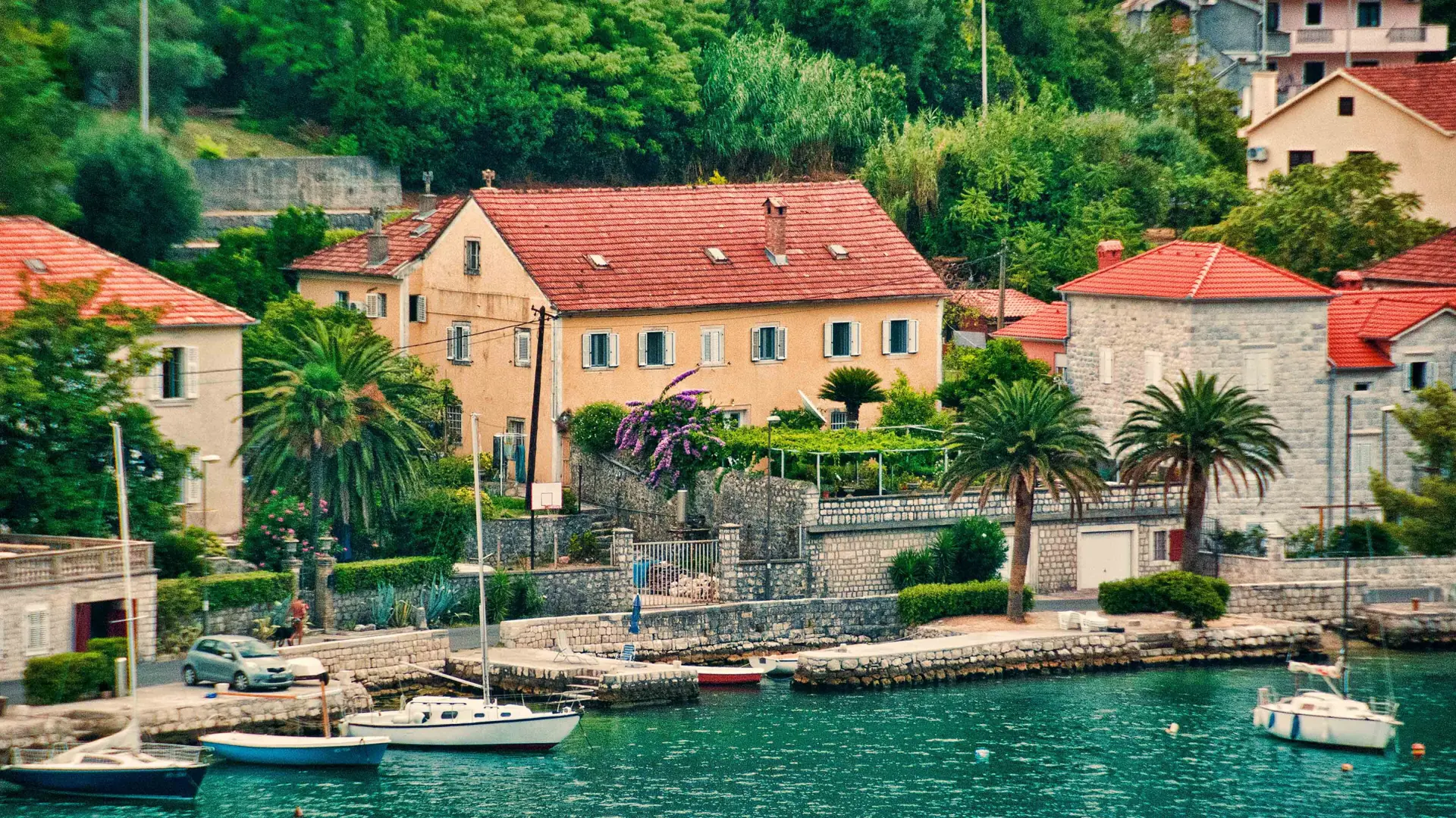 A yellow stone house and small boats on the waterfront at Dobrota